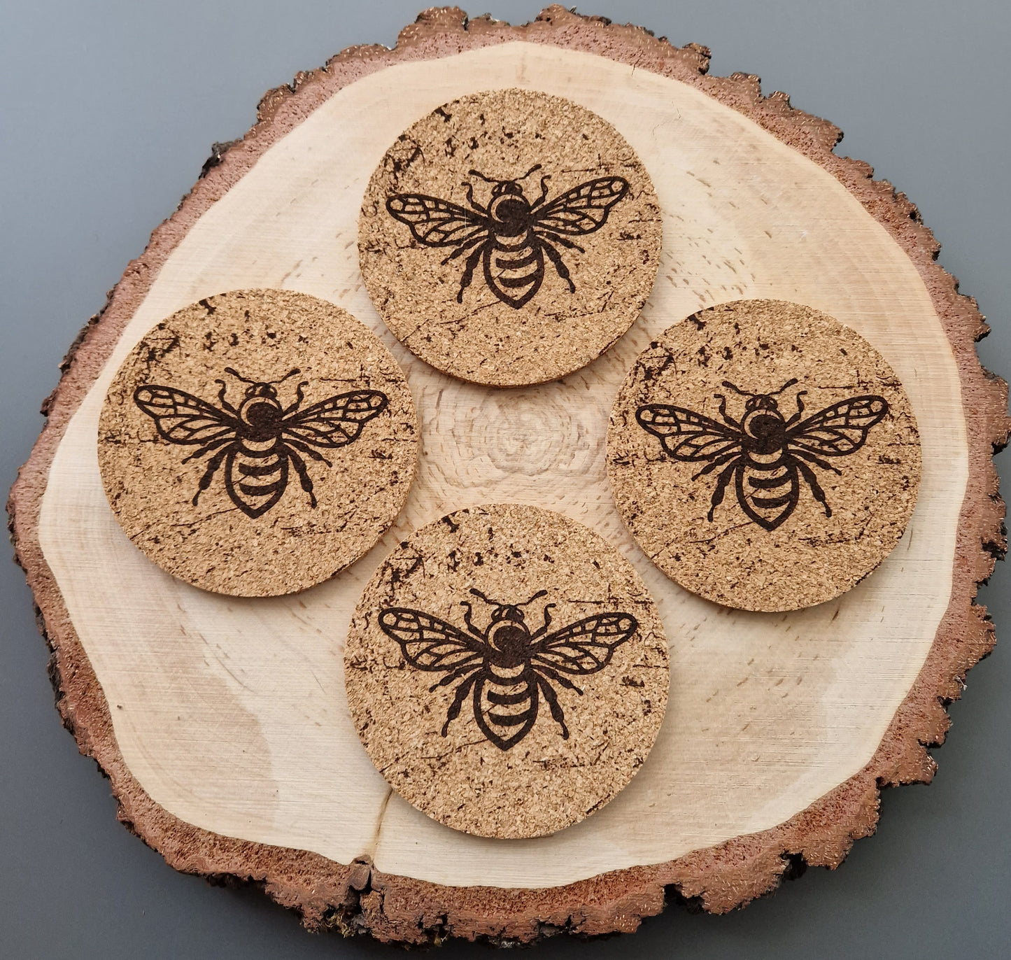 round cork coasters with a distressed bee design displayed on a log slice