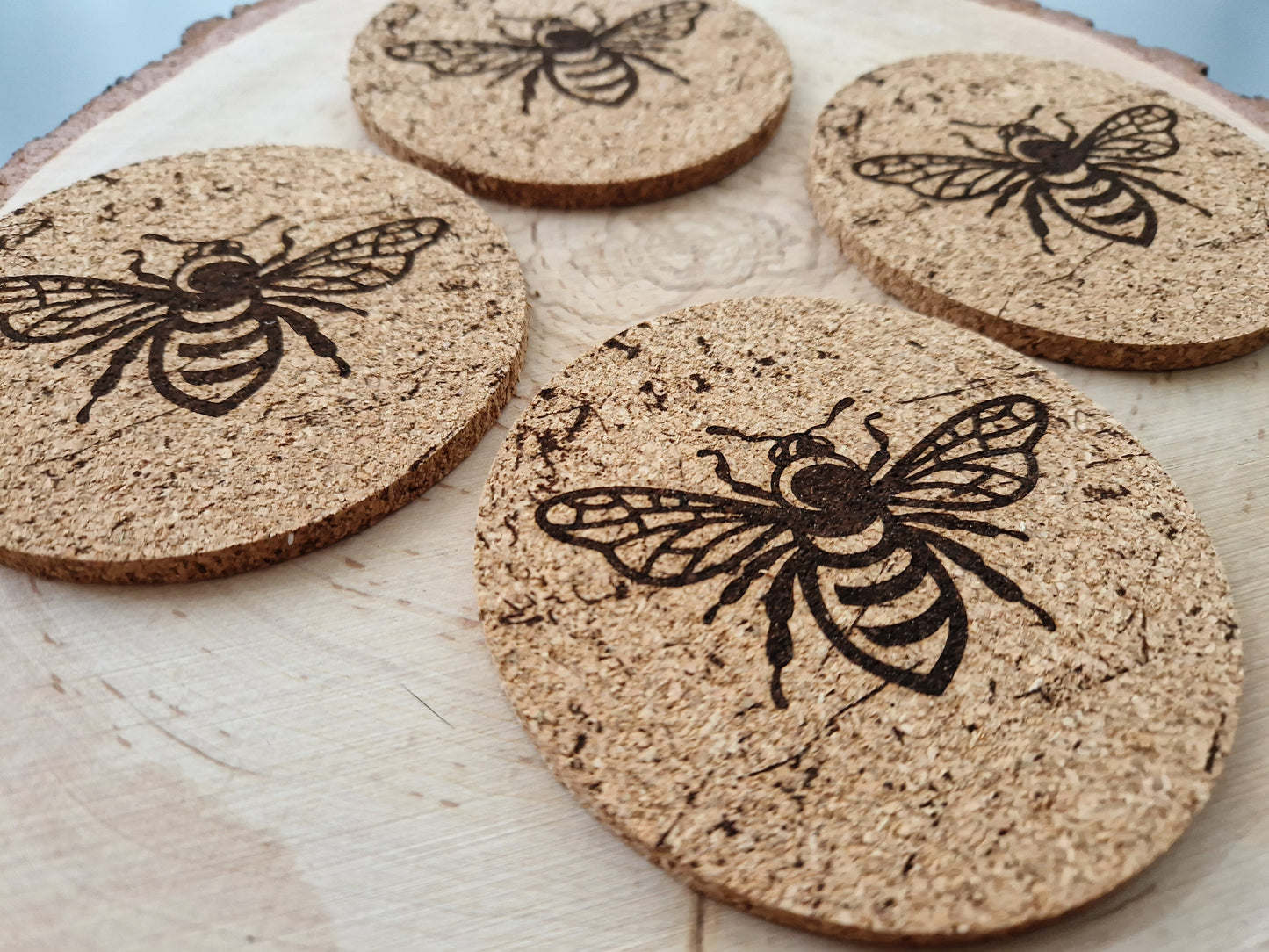 round cork coasters with a distressed bee design displayed on a log slice