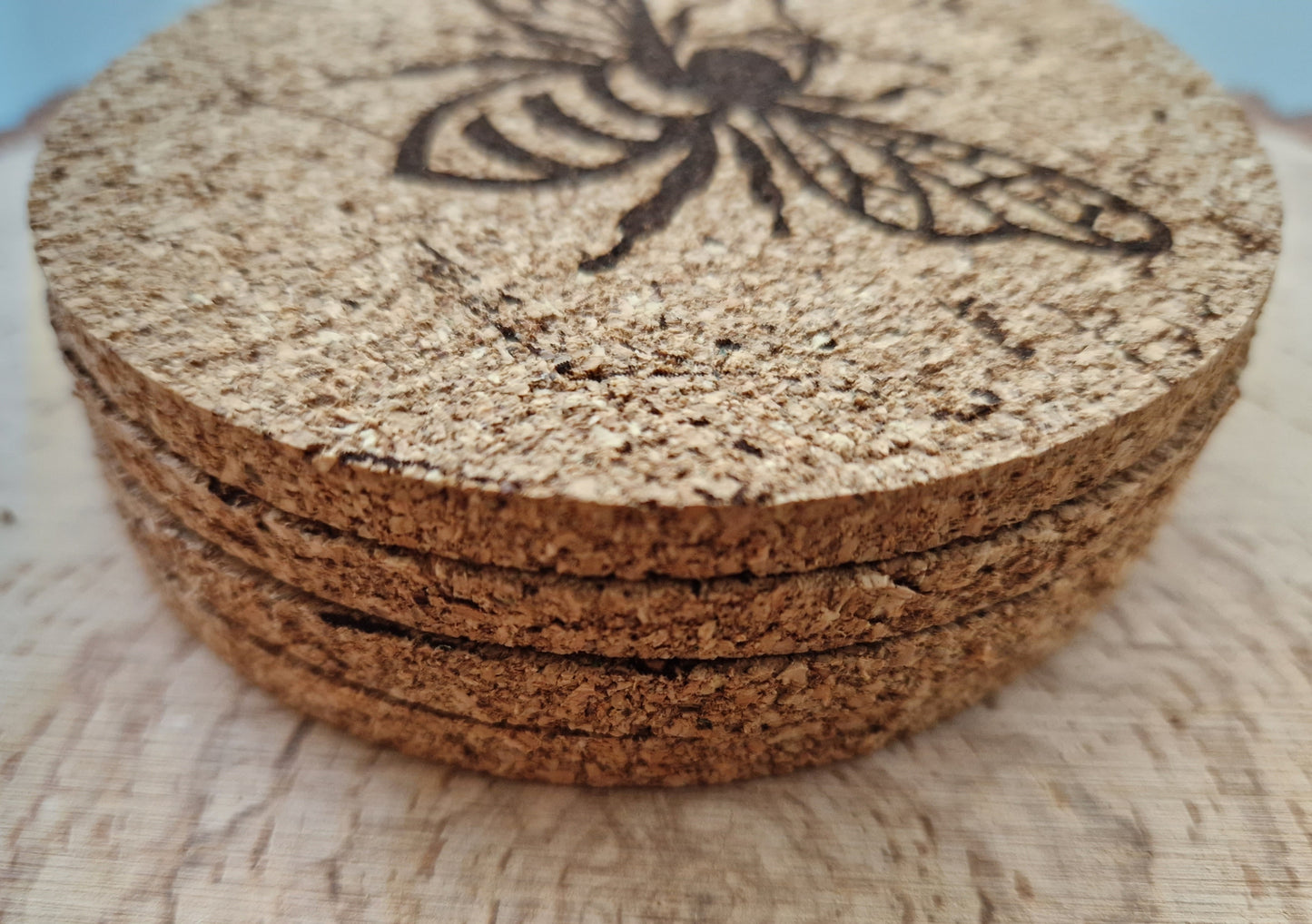 round cork coasters with a distressed bee design displayed on a log slice