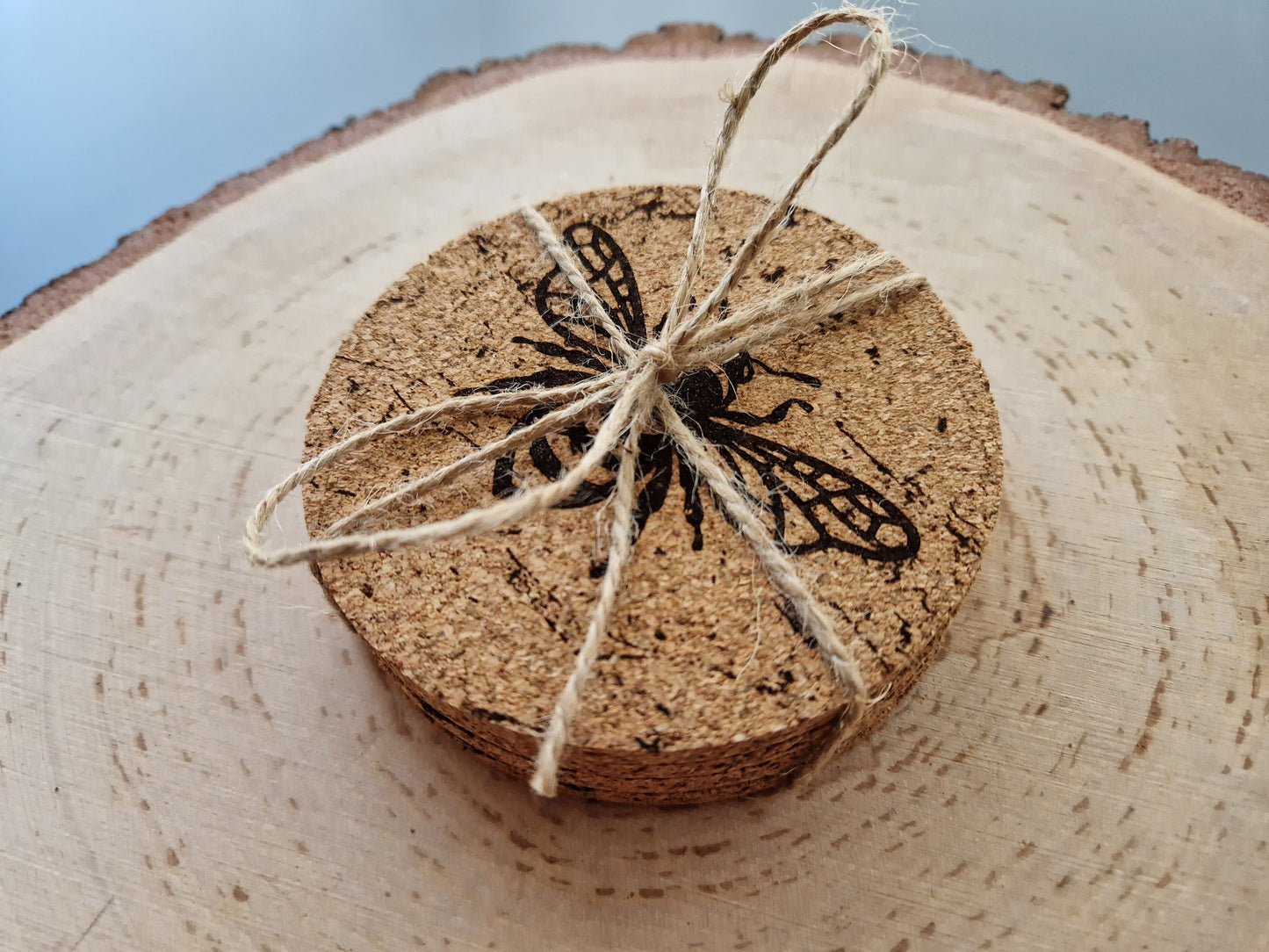 round cork coasters with a distressed bee design displayed on a log slice