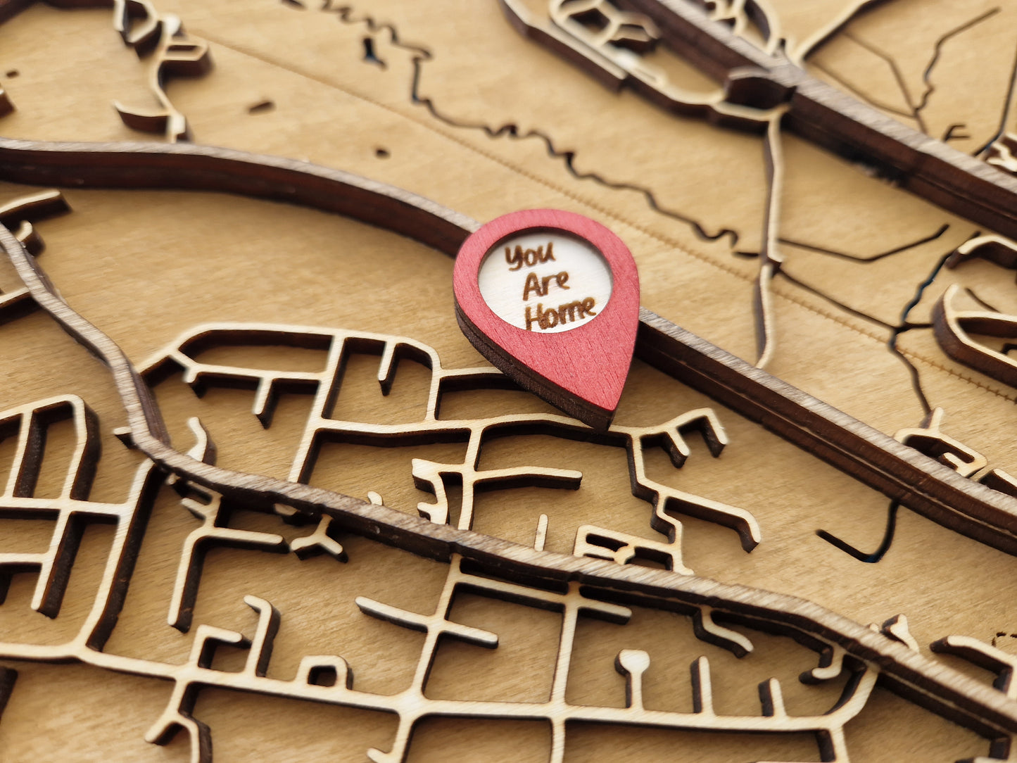 Layered wooden map with intricate details and a red location marker that reads "You Are Home".