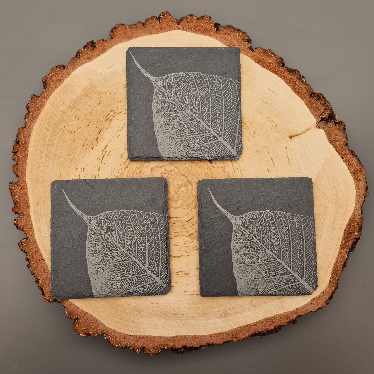 Square slate coasters with intricate leaf vein design displayed on wooden background