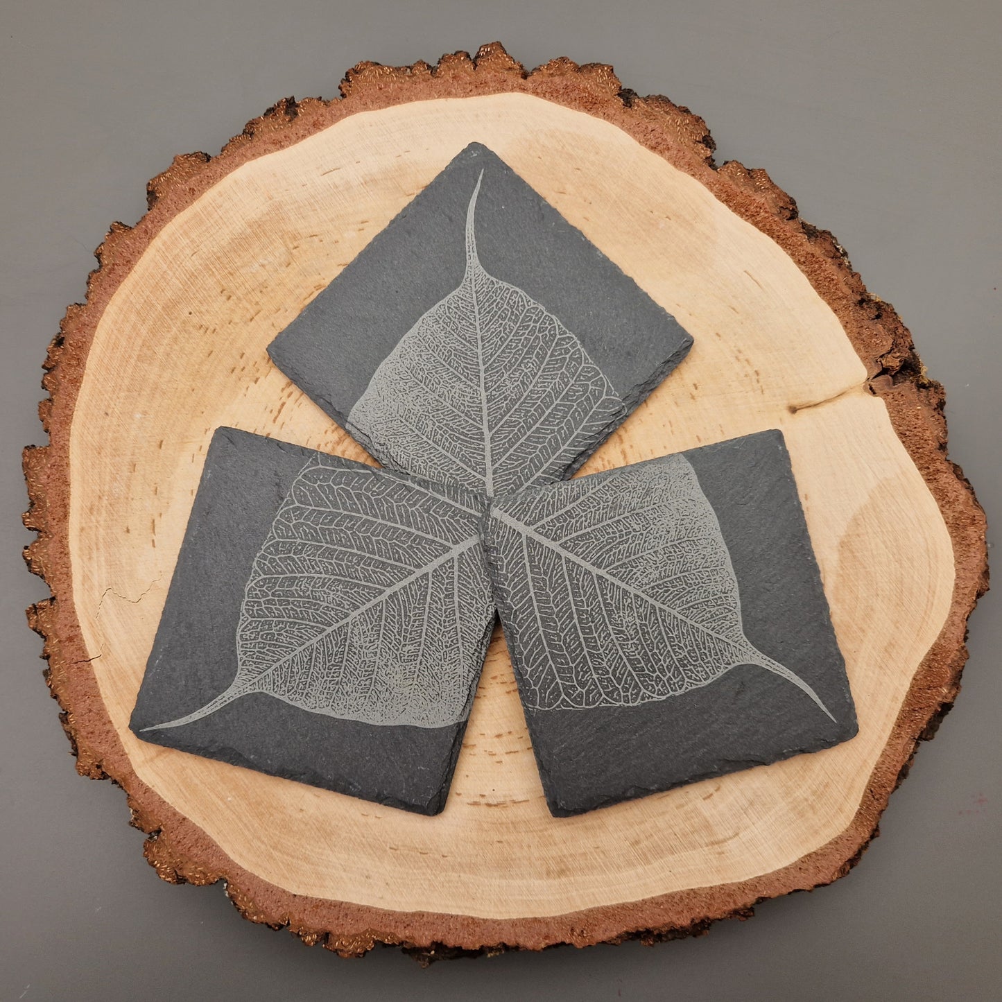 Square slate coasters with intricate leaf vein design displayed on wooden background