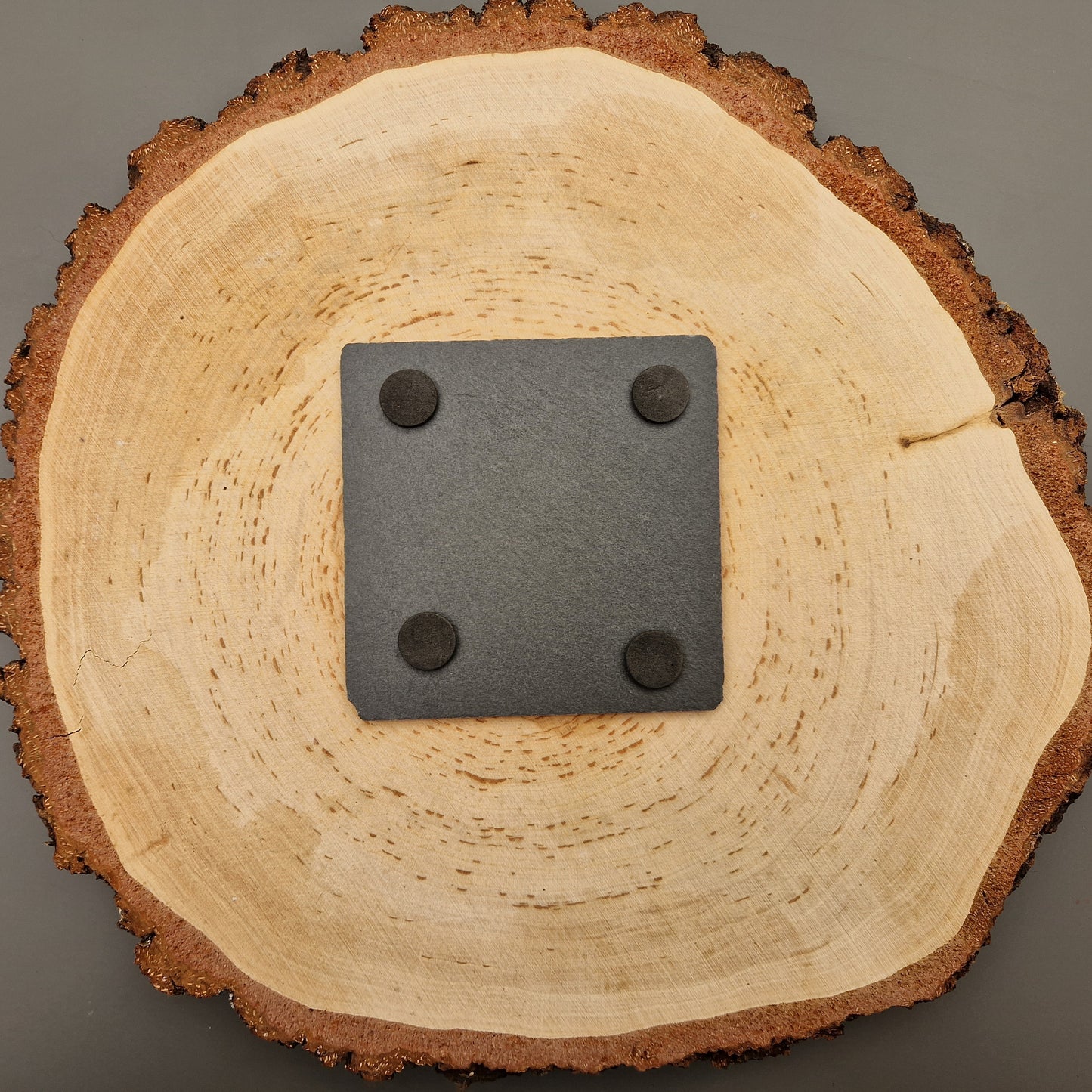 Back of square slate coasters with intricate leaf vein design displayed on wooden background