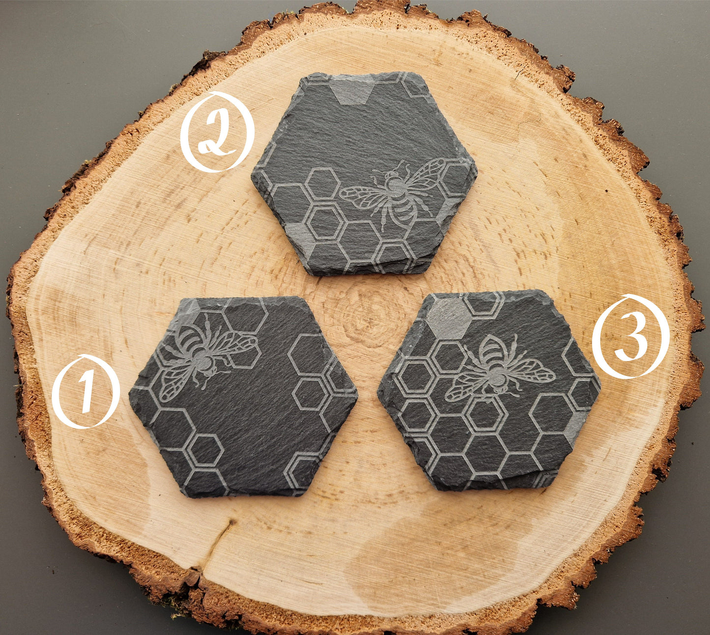 Hexagonal slate coasters with geometric honeycomb and bee design displayed on wooden background