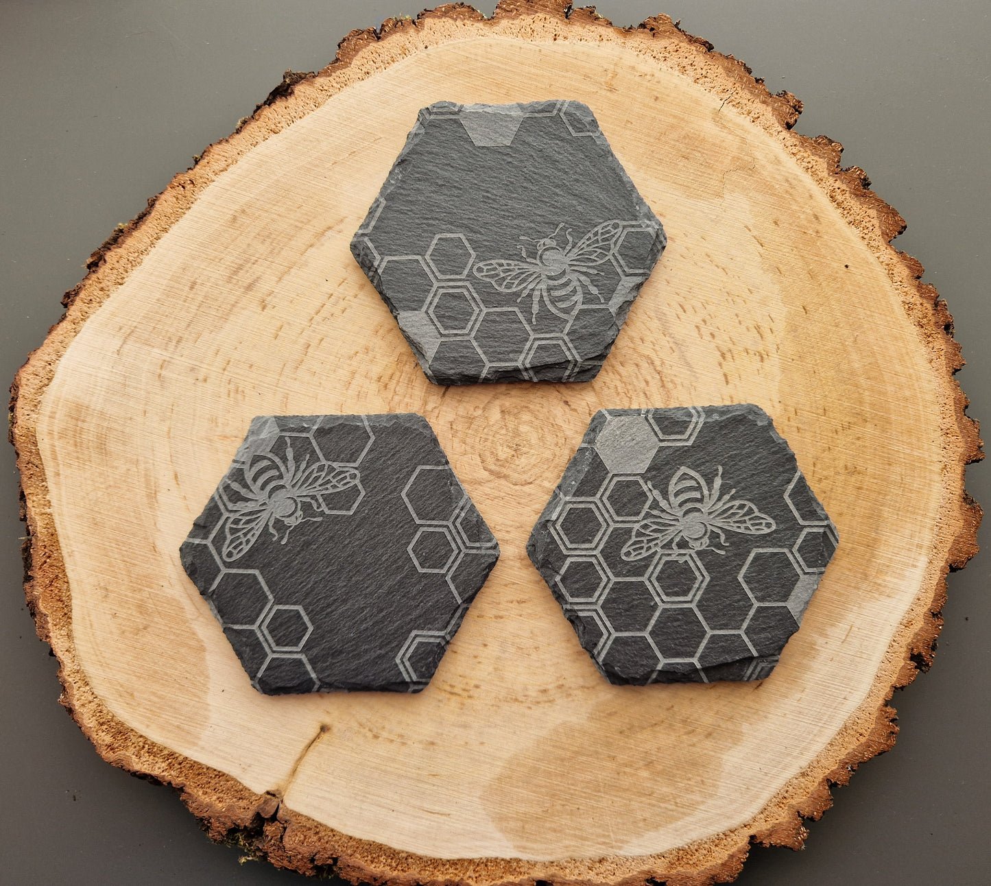 Hexagonal slate coasters with geometric honeycomb and bee design displayed on wooden background