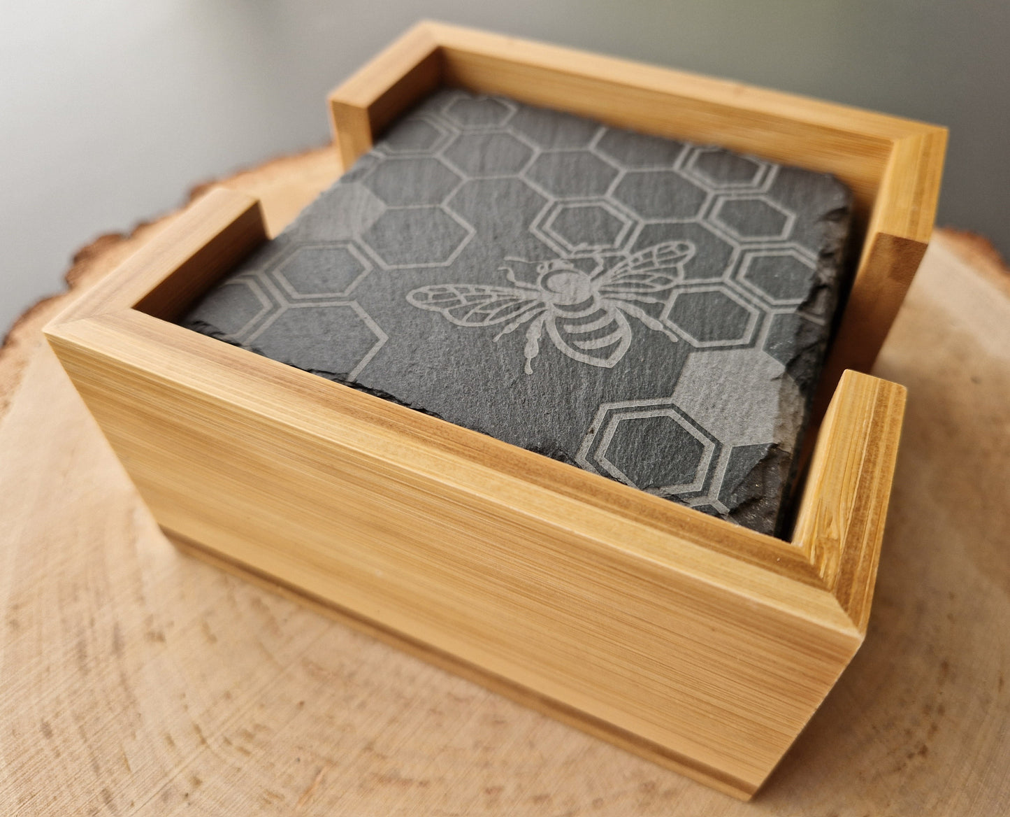 Square slate coasters with geometric honeycomb and bee design in bamboo box displayed on wooden background