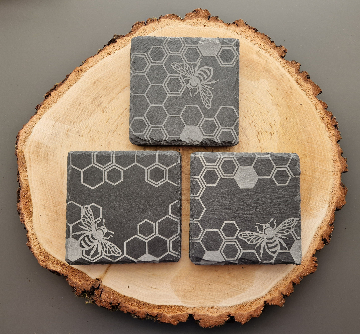 Square slate coasters with geometric honeycomb and bee design displayed on wooden background