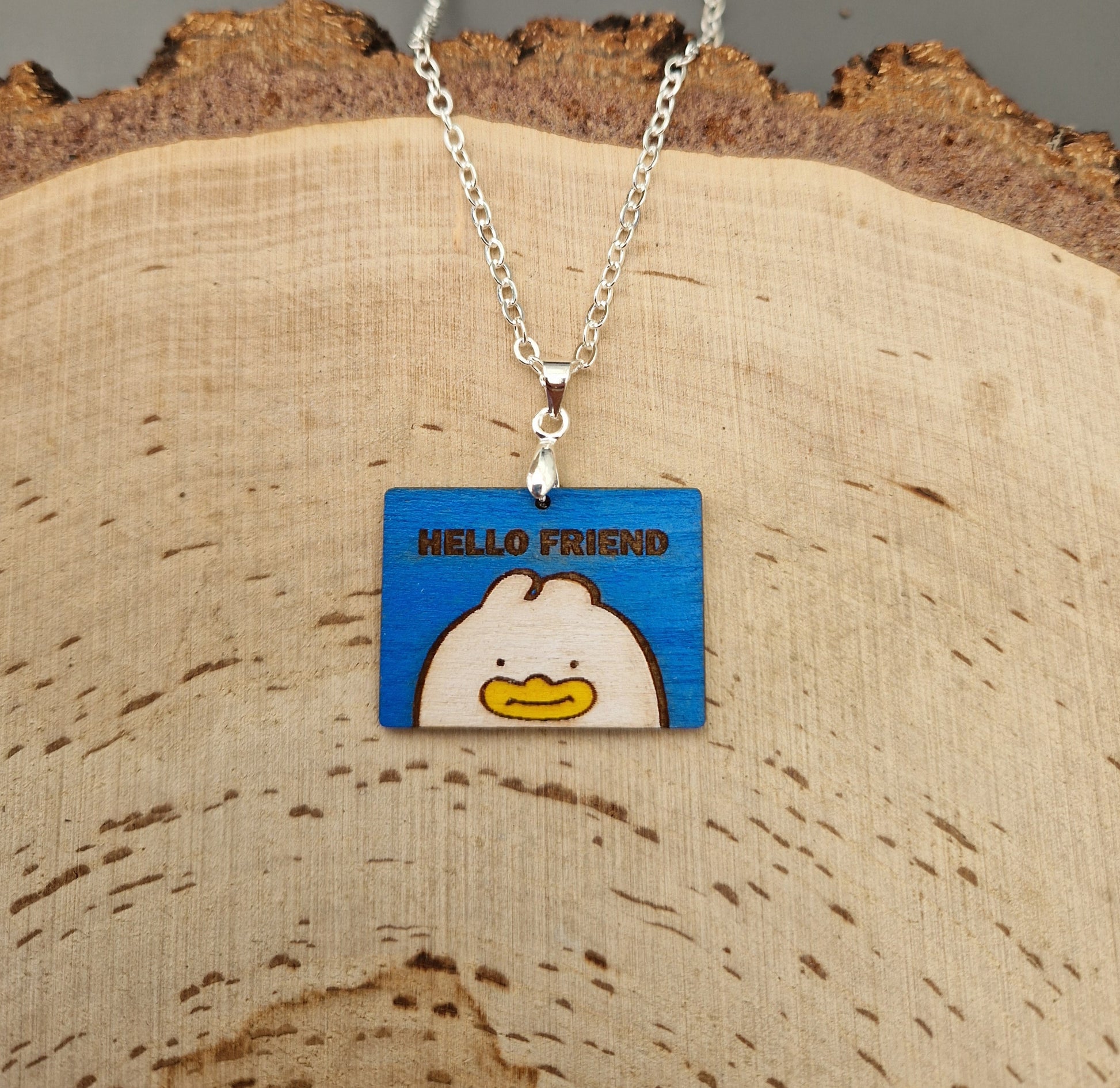 Necklace with a blue pendant featuring a kpop demon hunter Hello Friend character on a wooden surface