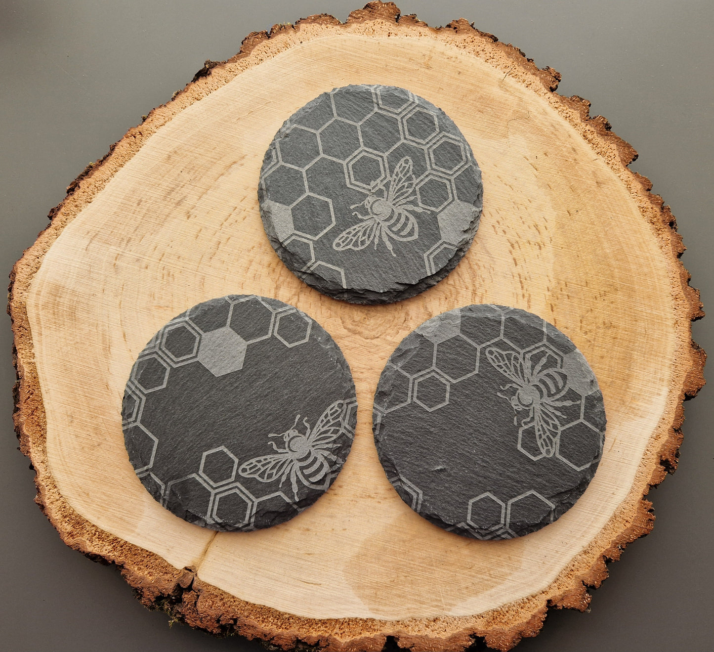 Round slate coasters with geometric honeycomb and bee design displayed on wooden background