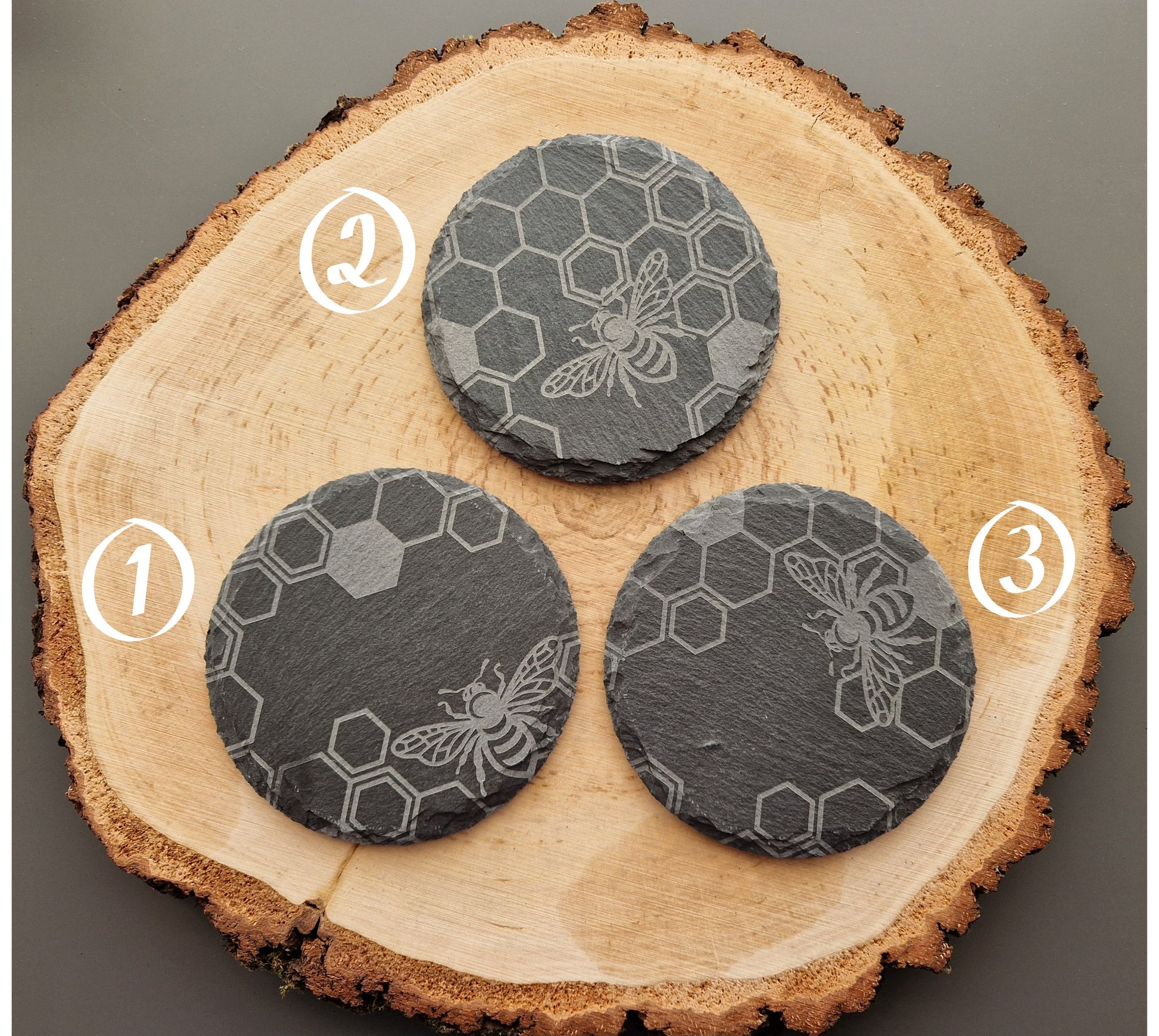 Round slate coasters with geometric honeycomb and bee design displayed on wooden background